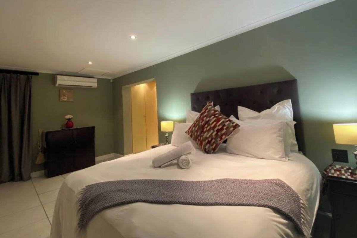 A hotel room with a large bed, a headboard, two bedside lamps, an air conditioning unit, a wardrobe, and a curtain.