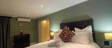 Une chambre d’hôtel avec un grand lit, une tête de lit, deux lampes de chevet, un appareil de climatisation, une armoire et un rideau.