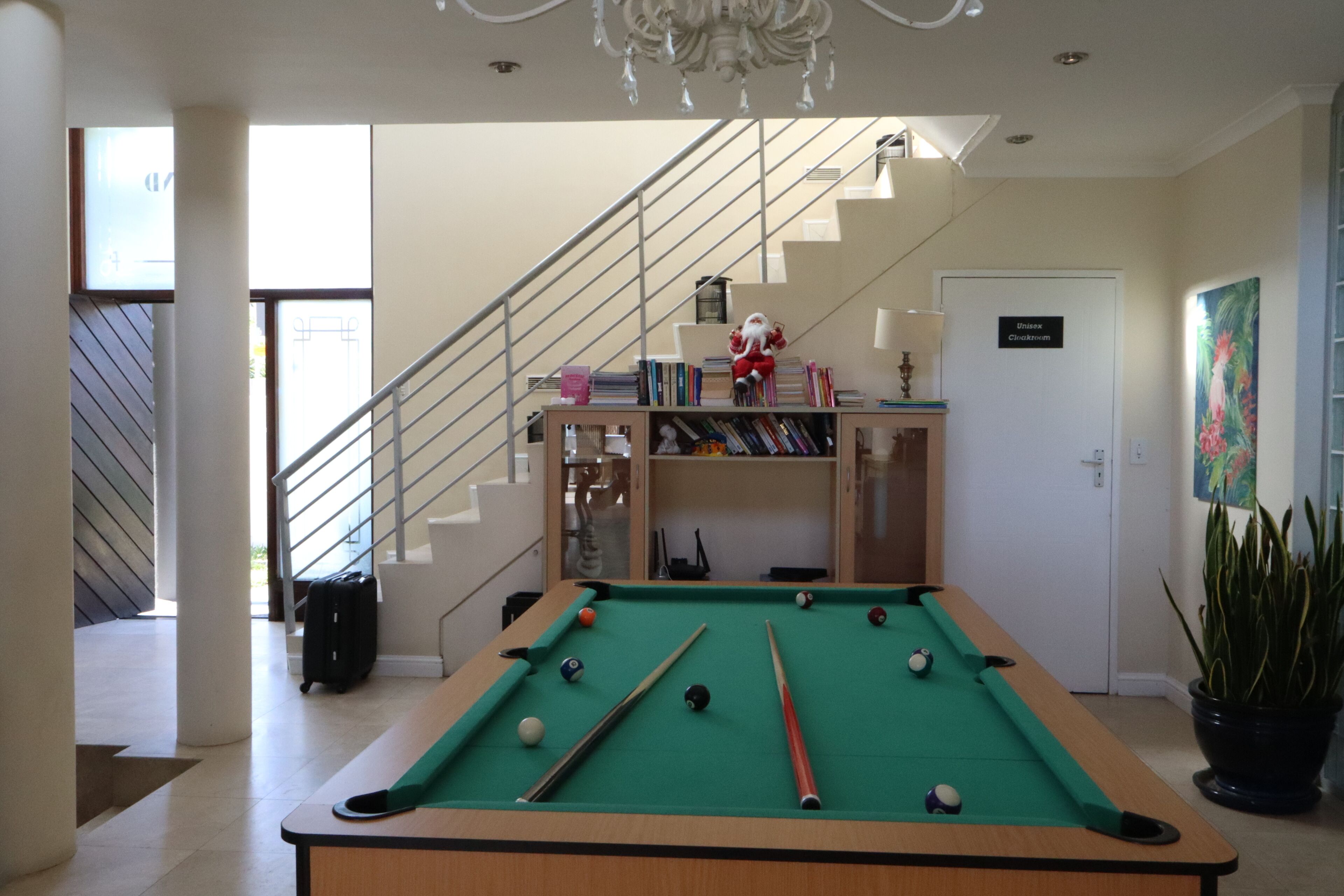A pool table in a room with a staircase, a bookshelf, and a door labeled "Unisex Children's".