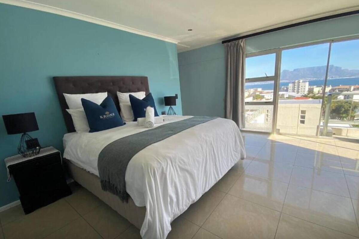 A hotel room with a large bed, two nightstands, a view of the city through large windows, and a balcony.