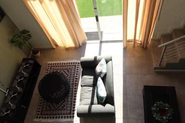 A living room with a sofa, a patterned rug, a coffee table, and a potted plant. - Imany Guesthouse (Cape Town)