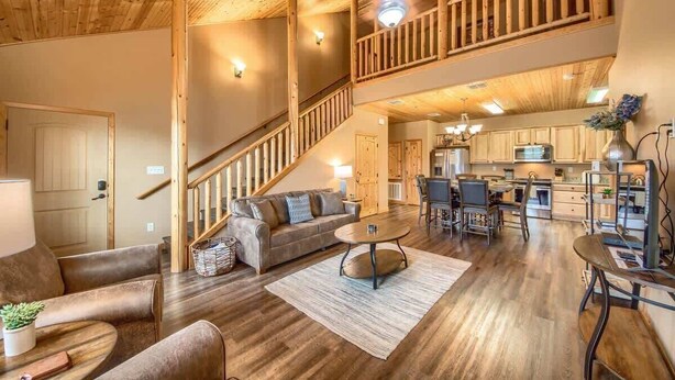 A spacious living area with a wooden staircase, a sofa, a coffee table, and a kitchen area with cabinets and a dining table.