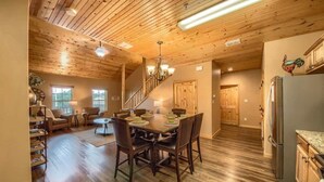 A spacious living area with a wooden ceiling, a dining table with chairs, a sofa, and a staircase leading to another level.