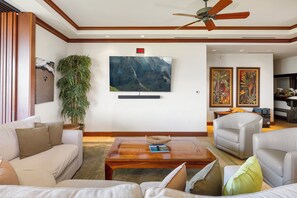 A living room with a flat-screen TV, a ceiling fan, a large plant, and two framed artworks.