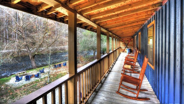 A covered porch with wooden beams and railings, overlooking a river with trees and boats.