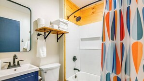 A bathroom with a white sink, toilet, and bathtub. There is a shelf with towels and a shower curtain with a geometric pattern.