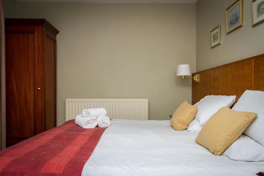 Ein ordentlich gemachtes Bett mit weißer und beiger Bettwäsche, einer rot-weiß gestreiften Decke und einem zusammengerollten Handtuch am Rand.