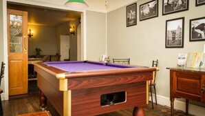 A pool table in a room with wooden flooring, a door, and a wall with framed pictures. - Woolpack Inn (Holmrook)