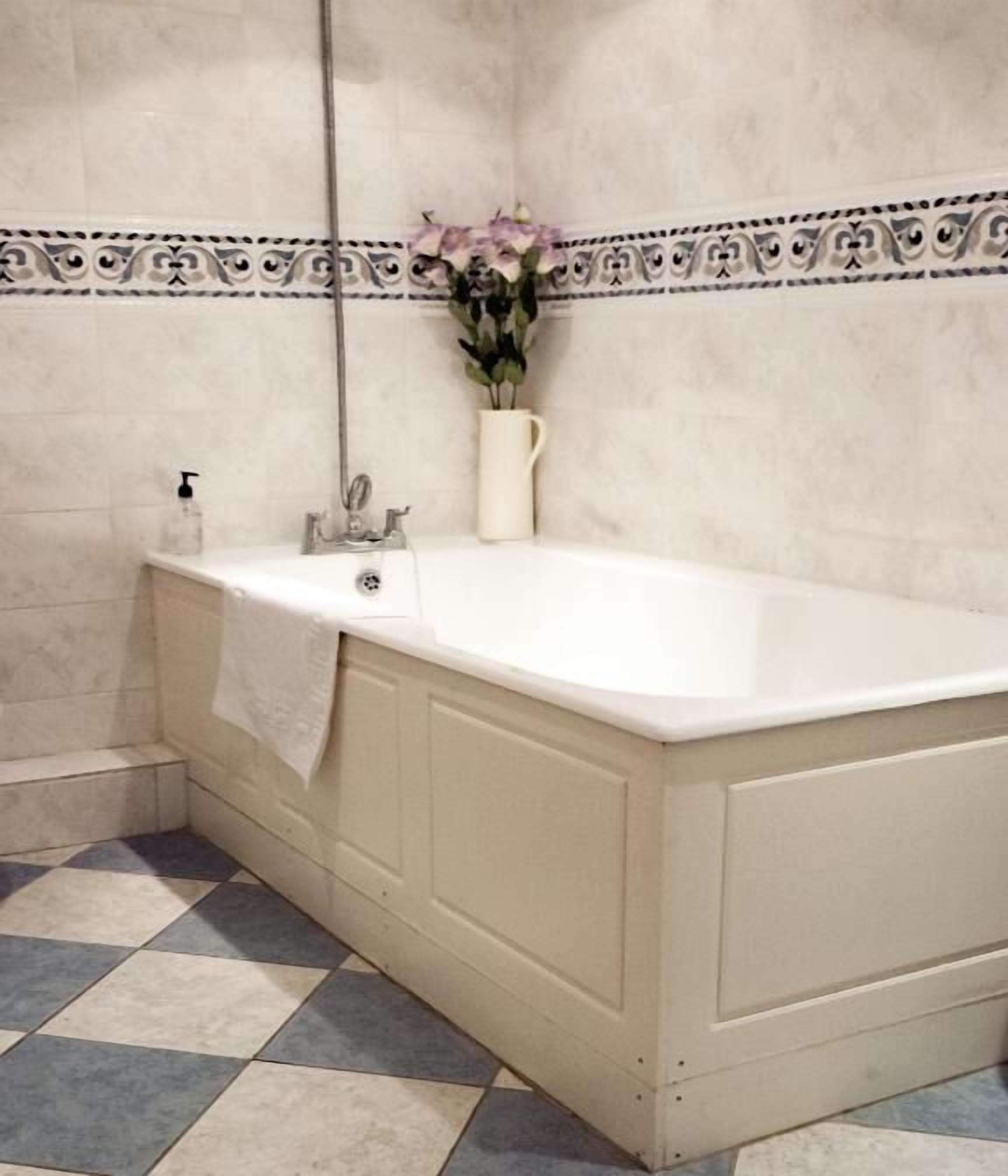 A bathroom with a white bathtub, a white towel hanging on the wall, and a vase with flowers.