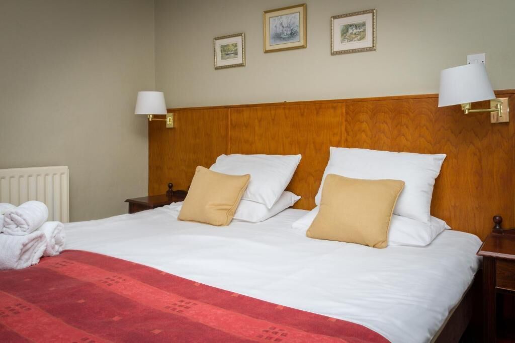 A hotel room with a wooden headboard, white bedding, and two bedside lamps.