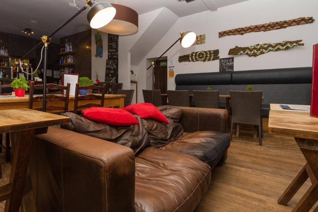 A cozy restaurant interior with a leather couch, wooden tables, and modern lighting fixtures.
