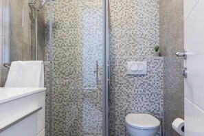 Une salle de bain moderne avec une douche à parois de verre, des toilettes et un lavabo blanc.