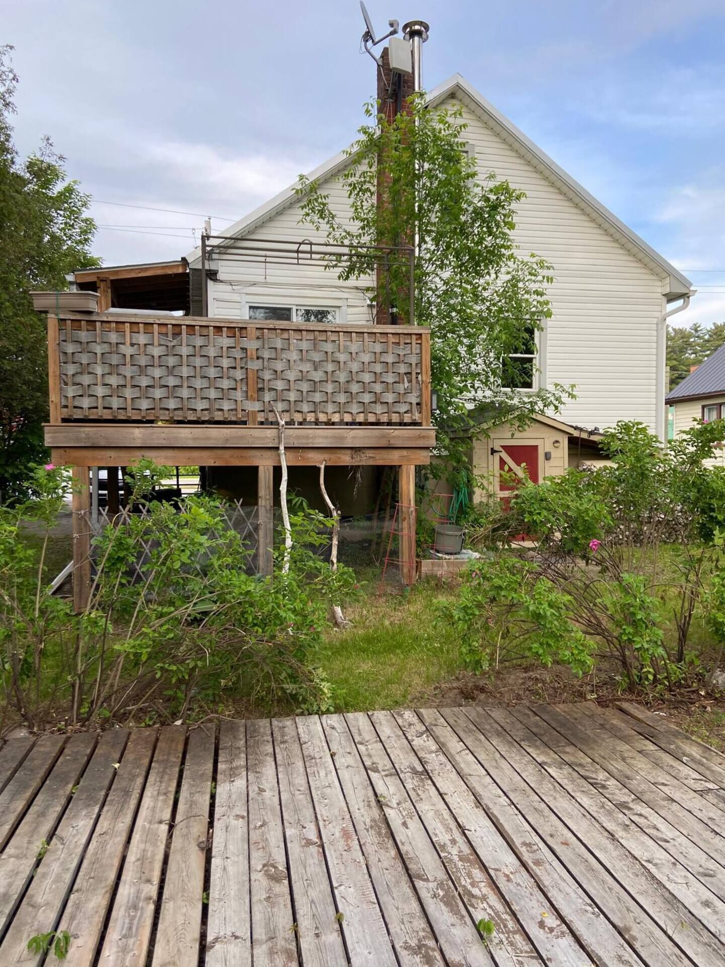 Ein Haus mit einer Holzdar Terrasse, einem umzäunten Bereich mit Pflanzen und einer Satellitenschüssel auf dem Dach.