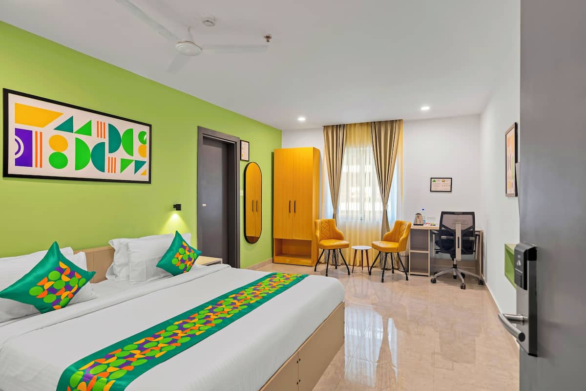 A hotel room with a bed, a desk, two chairs, a television, and a green wall with artwork.