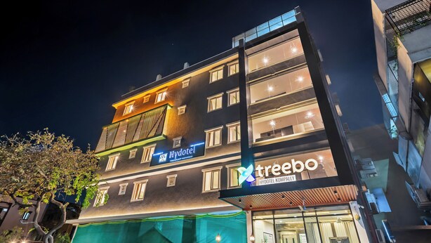 Ein mehrstöckiges Gebäude mit einem 'Hydotel'-Schild und einem 'treebo'-Schild, das ein Hotel und ein Unternehmen kennzeichnet.