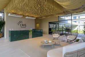 A reception area with a green reception desk, wicker chairs, a white sofa, and a ceiling with hanging lights. - Cais Ecoresidencia Luxo em Muro Alto (Ipojuca)