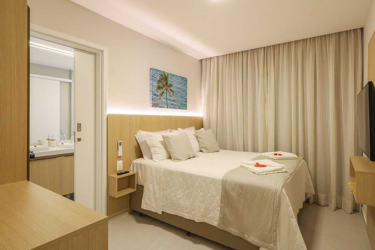 A hotel room with a bed, bedside tables, a mirror, a painting, and a TV.