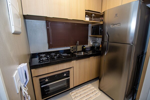 A compact kitchen with a built-in oven, a stainless steel refrigerator, and a microwave. - Cais Ecoresidencia Luxo em Muro Alto (Ipojuca)