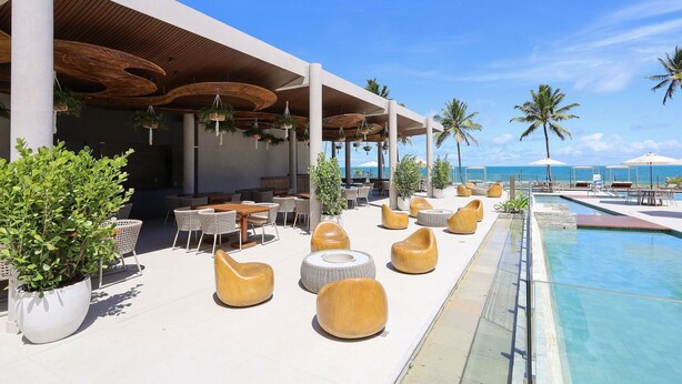 A poolside area with lounge chairs, a pool, and a view of the ocean.