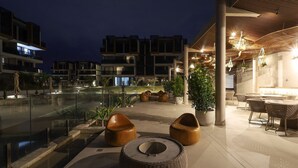 A modern outdoor lounge area with seating, a glass barrier, and a view of adjacent buildings.