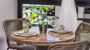 A dining table with a view of a pool, wicker chairs, and a bottle of water.