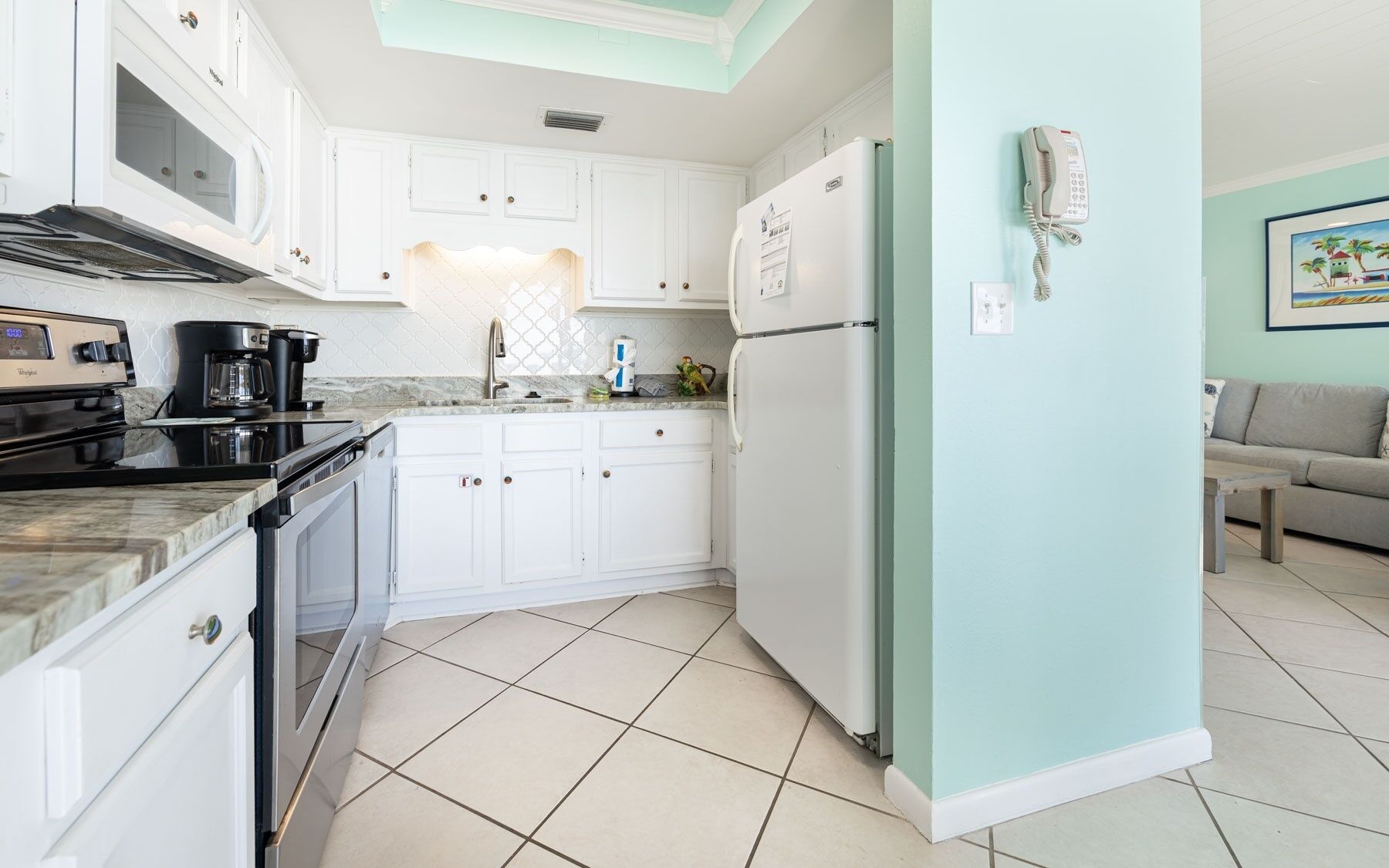 A kitchen with white cabinets, a black stove, and a white refrigerator. There is a microwave above the stove, a coffee maker, and a sink with a faucet.