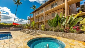 A hotel with a pool area, including a hot tub and lounge chairs, surrounded by tropical plants and a clear blue sky. - Kihei Ali'i Kai D108 2 Bedroom Condo (Kihei)