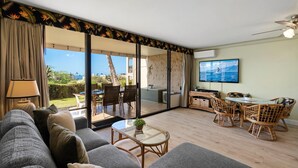A spacious living room with a large sliding glass door leading to an outdoor area, a comfortable sofa set, a dining table with chairs, and a ceiling fan. - Kihei Ali'i Kai D108 2 Bedroom Condo (Kihei)