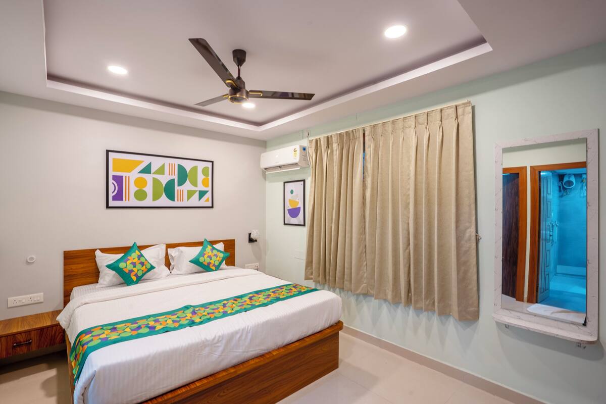 A modern hotel room with a large bed, ceiling fan, air conditioning unit, and a window with curtains.