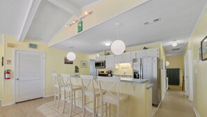 A kitchen with a central island, white bar stools, a microwave, a refrigerator, and a sink. - Book A Key West Heart | Semi-Oceanfront Sandbridge Rental (Virginia Beach)