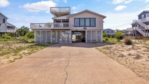 A two-story house with a balcony, a garage, and a sandy driveway. - Book A Key West Heart | Semi-Oceanfront Sandbridge Rental (Virginia Beach)