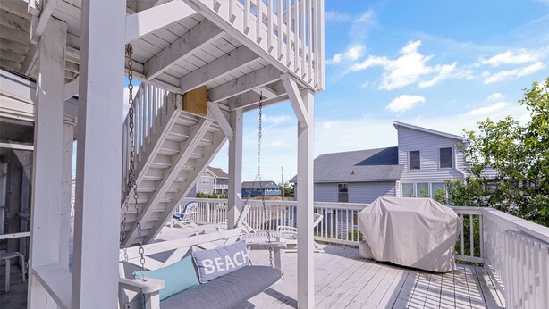 A wooden deck with a swing set, a covered grill, and a view of a house in the background. - Book A Key West Heart | Semi-Oceanfront Sandbridge Rental (Virginia Beach)