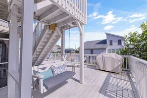 Une terrasse en bois avec une balançoire, un barbecue couvert et une vue sur une maison au loin.