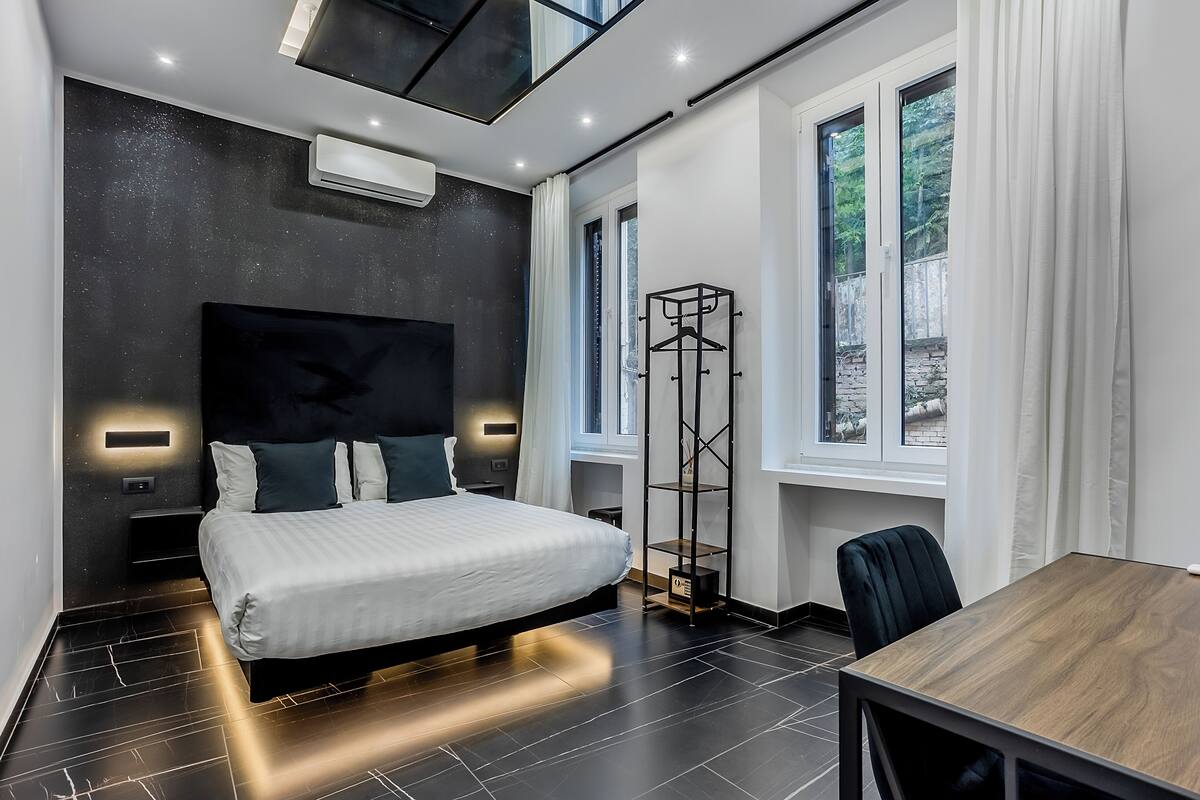 A modern bedroom with a large bed, a desk, and a wardrobe.
