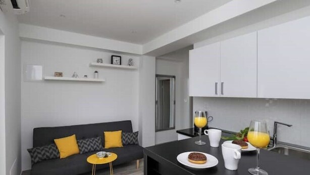 A modern kitchen with white cabinets, a black countertop, and a dining area with a sofa and a small round table.