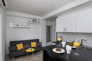 Una cocina moderna con armarios blancos, encimera negra y un comedor con sofá y una mesa redonda pequeña.