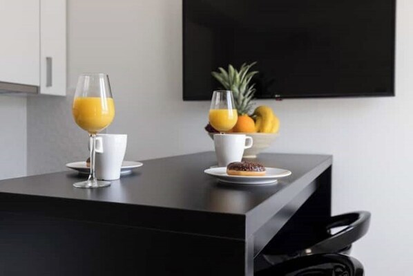 Una cocina moderna con encimera negra, una taza blanca, un vaso de zumo de naranja, un plato con una rosquilla y un bol de fruta, incluyendo piña y plátanos.