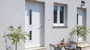 A building with white exterior walls, two windows with white frames, and a small table with chairs outside.