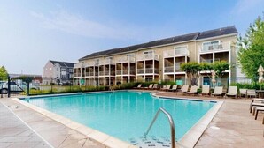Une piscine dotée d’une plage carrelée, entourée d’un bâtiment avec des balcons et une clôture.