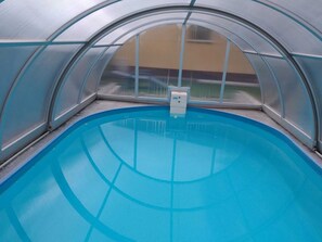 An indoor swimming pool with a clear, blue water surface, surrounded by a curved, transparent roof structure.