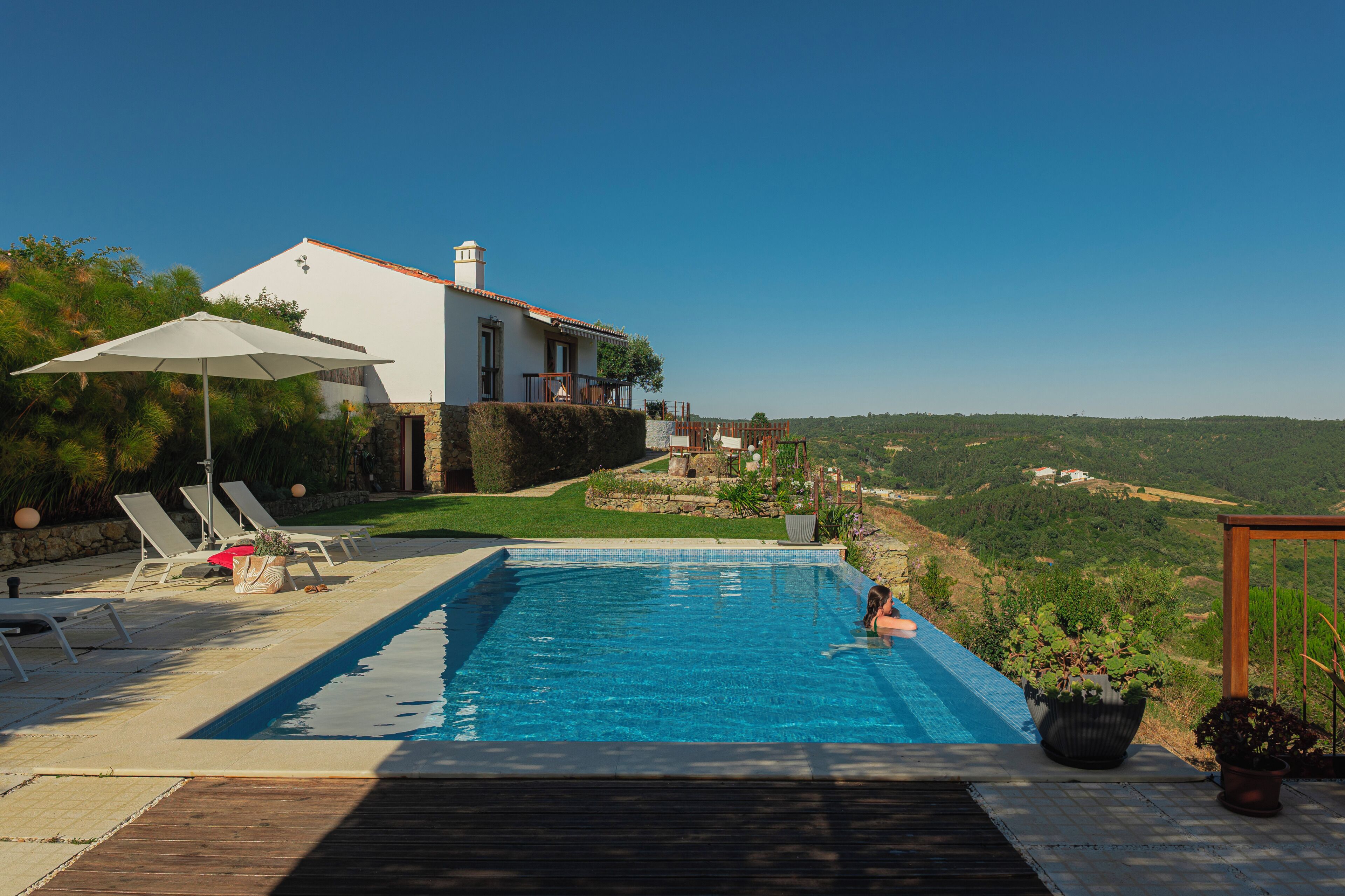Une piscine avec des chaises longues, une maison blanche et une vue sur la campagne.