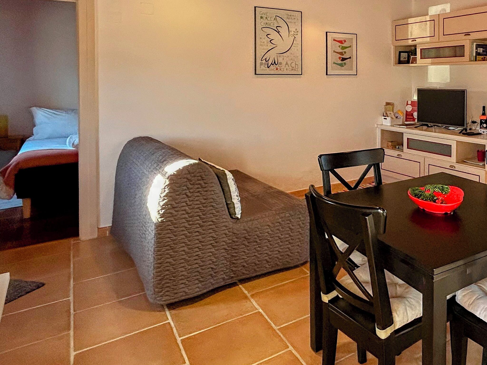 Un espacio habitable compacto con kitchenette, un comedor con mesa y sillas, y una cama al fondo.