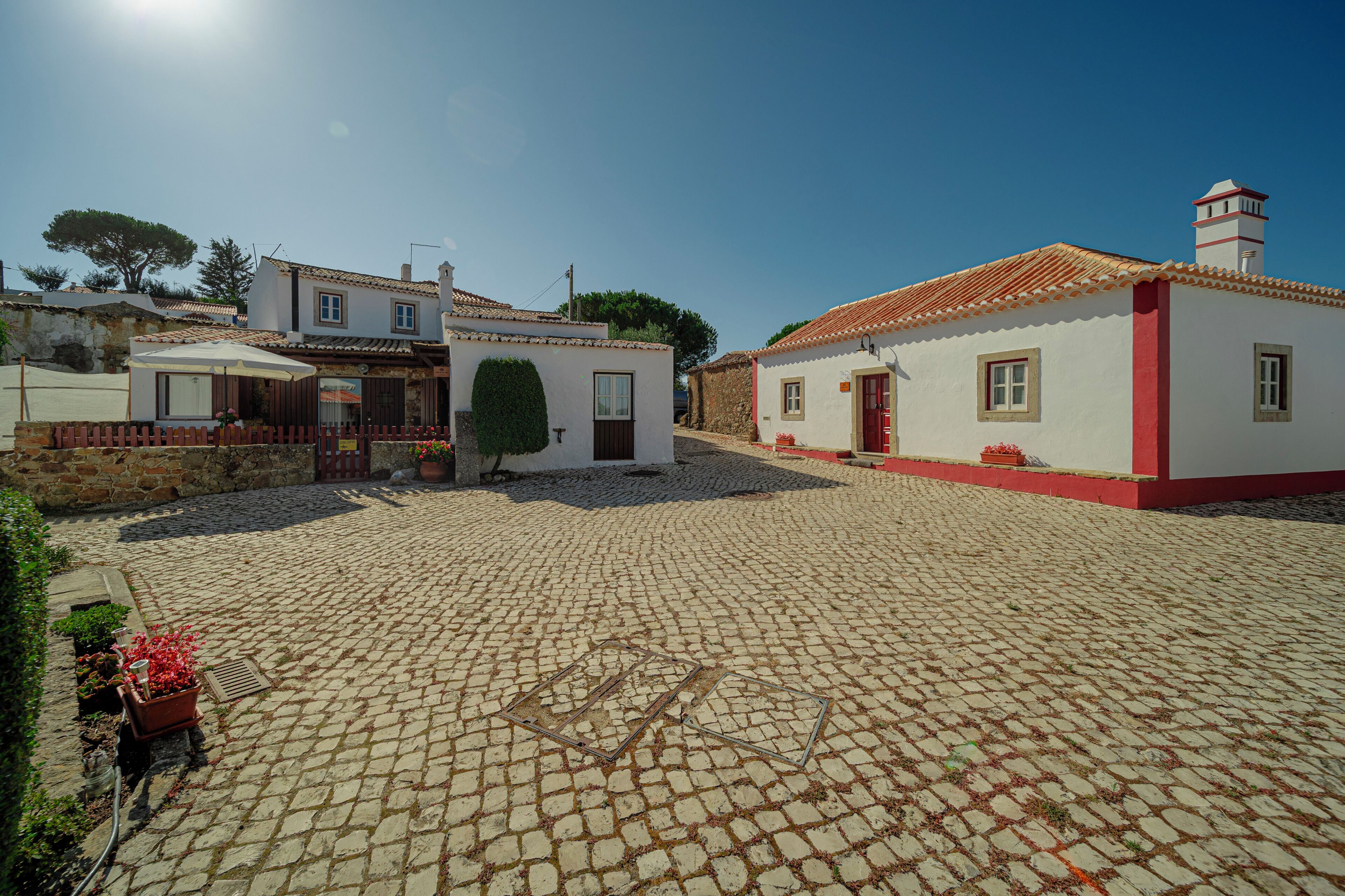 A cobblestone courtyard with buildings, a red door, and a white wall with a red stripe.