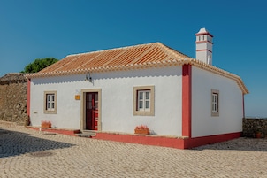 Un pequeño edificio blanco con puerta roja, ventanas y chimenea.