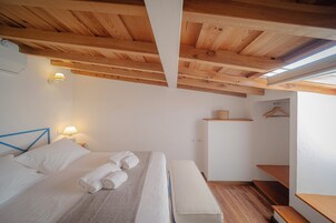 Un dormitorio con una cama, lámparas de noche, un banco de madera y un pequeño estante.