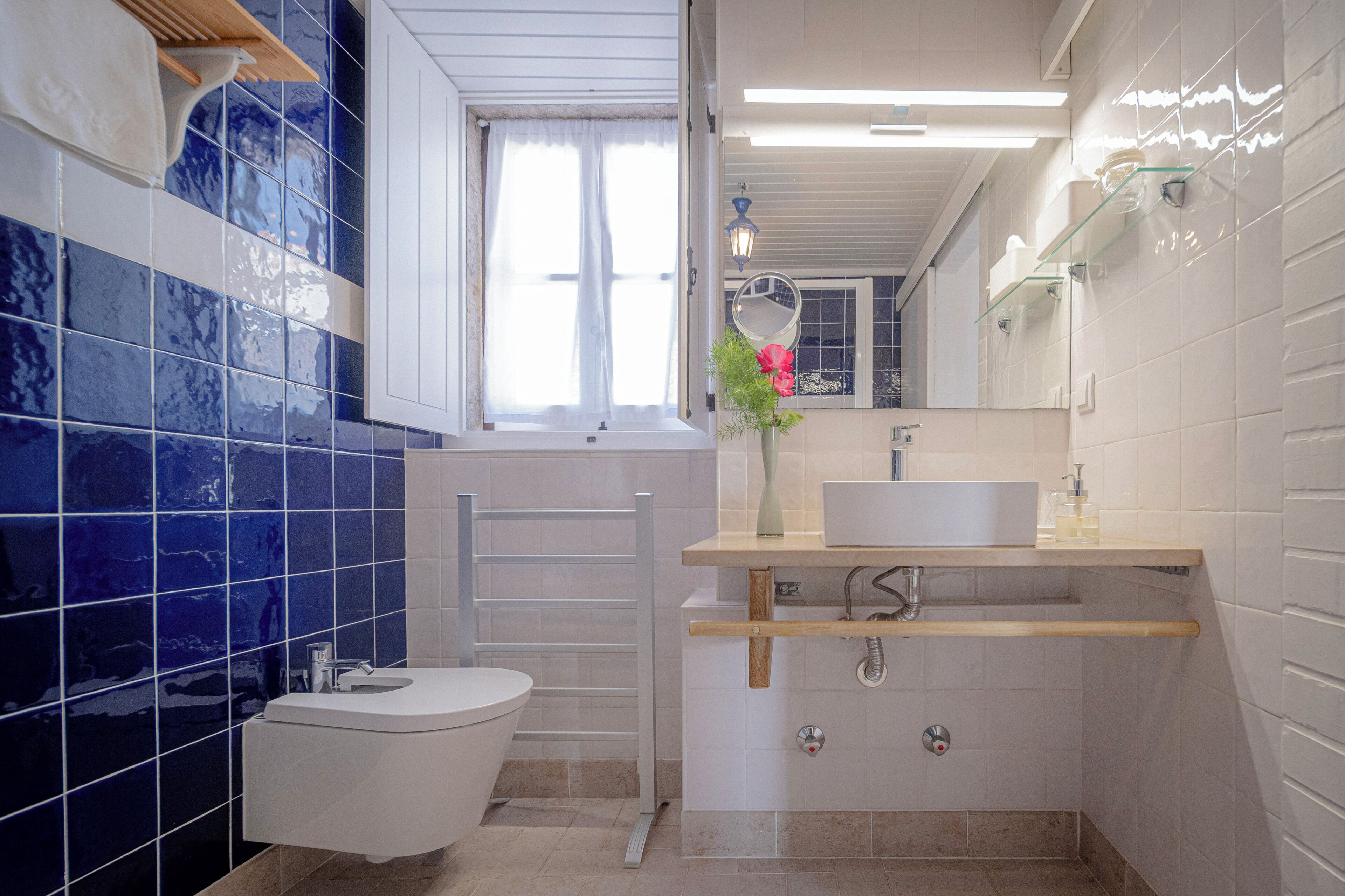 A bathroom with a toilet, sink, mirror, and a window with curtains.