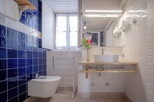 Un baño con inodoro, lavamanos, espejo y ventana con cortinas.