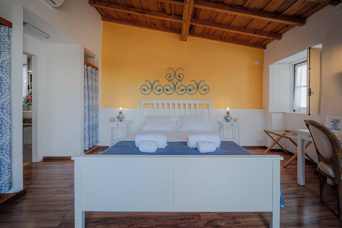 A bedroom with a wooden ceiling, a bed with white bedding, two bedside tables with lamps, and a decorative wall piece.