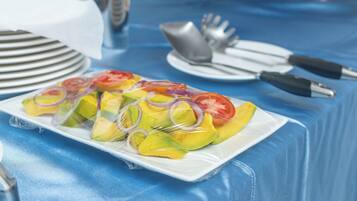 Une assiette de salade de fruits contenant de l’avocat, de la mangue, des tranches de tomate et d’oignon, le tout présenté sur une assiette blanche.