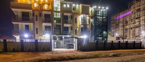 A multi-story building with a gated entrance, a parked vehicle, and a construction site in the background.